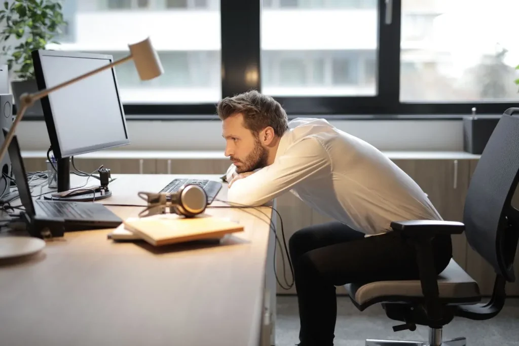 Personne assise penchée vers écran d’ordinateur, image illustrant la nécessité de corriger sa posture du dos au bureau.