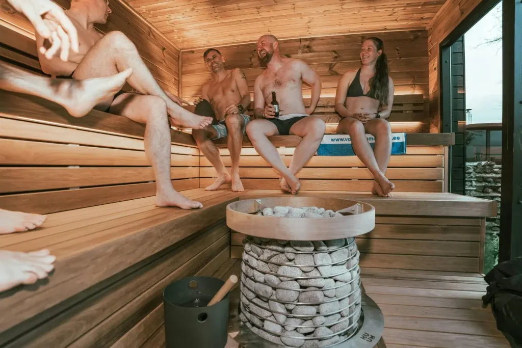 Quatre personnes assises dans un sauna en bois clair, image qui illustre la détente et les bienfaits de la chaleur sèche comparée au hammam.