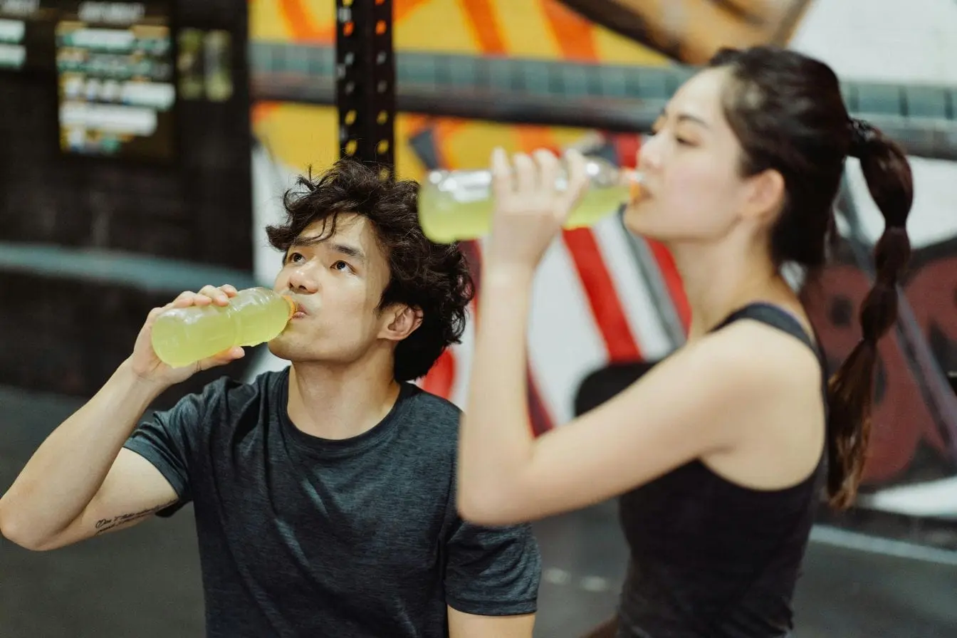 Deux sportifs hydratent leur corps avec boisson jaune, image illustrant l’énergie et la récupération offertes par une boisson aux électrolytes maison.
