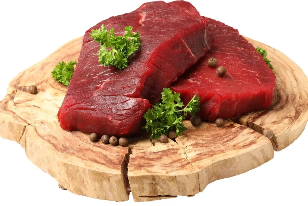 Deux morceaux de viande rouge sur planche bois, image illustrant les choix alimentaires contrastés avec les habitudes végétales des zones bleues.