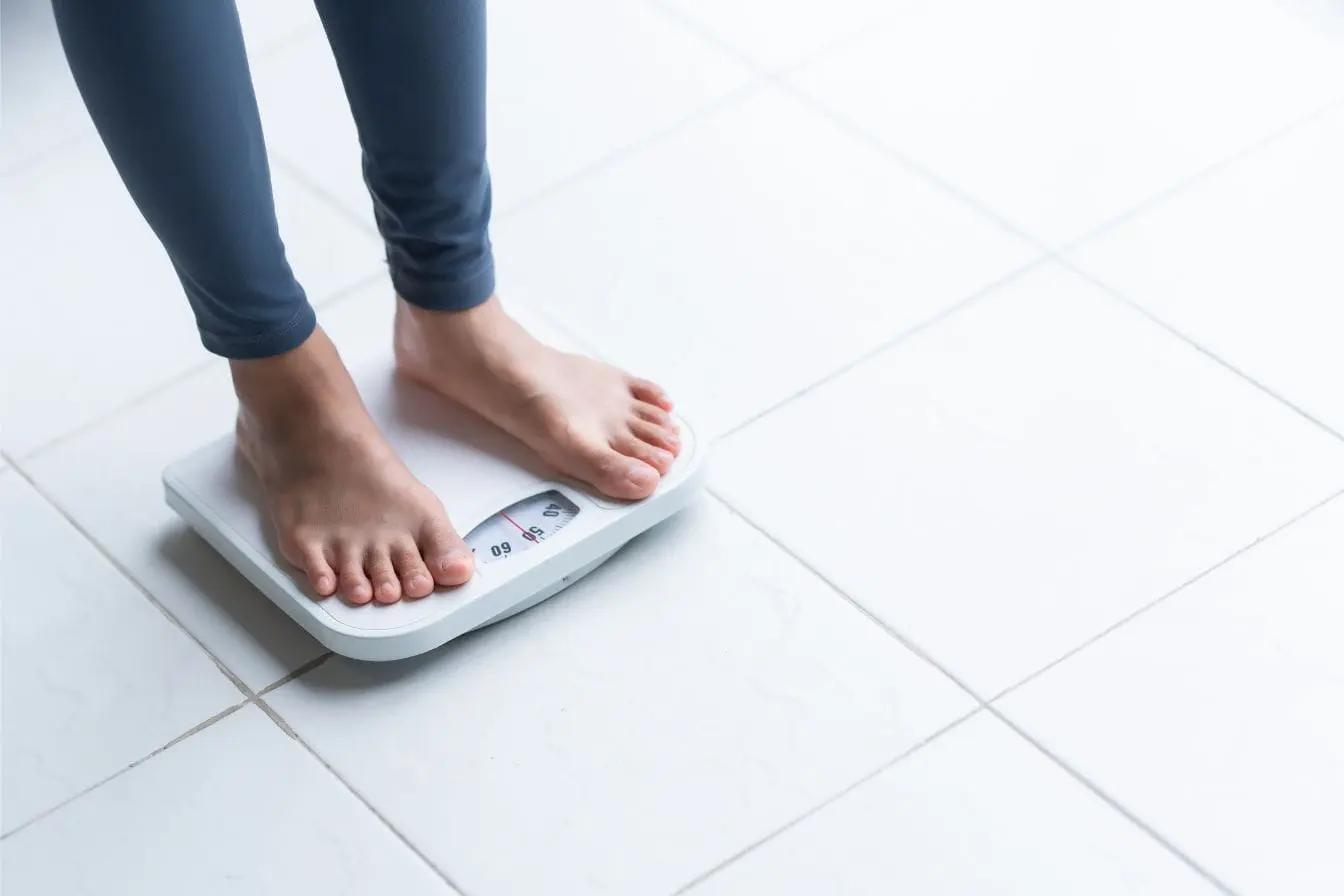 Balance mécanique Personne debout sur balance affichant environ 60 kilos, image qui illustre le plateau de perte de poids et la difficulté à voir l’aiguille bouger.