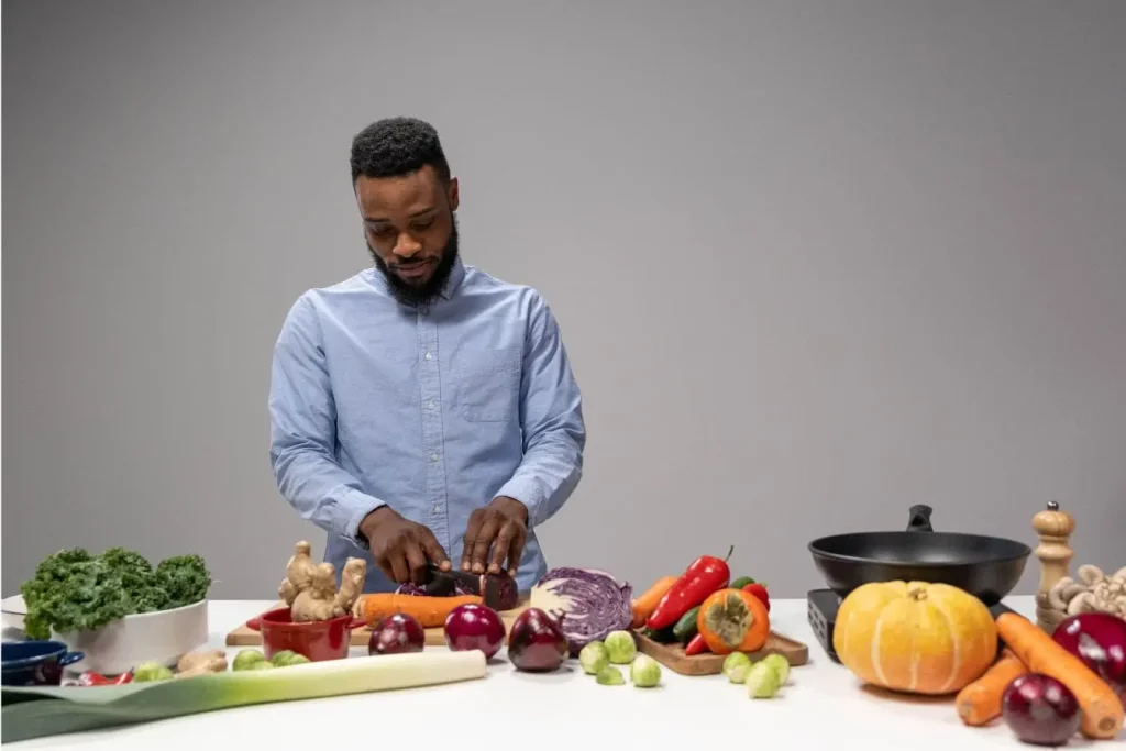 Personne coupant carotte sur planche entourée de légumes frais, image qui illustre le lien entre alimentation et fertilité masculine.