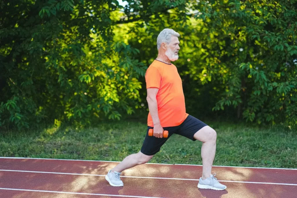 Personne en t‑shirt orange faisant une fente avec haltères sur piste extérieure, image qui illustre l’énergie et la vitalité du sport.