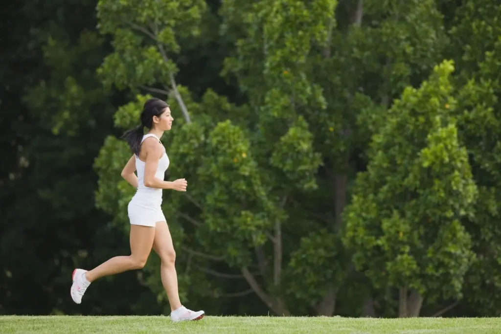 Personne en débardeur et short blanc courant dans parc, reflet de l’énergie apportée par une bonne alimentation avant l’effort sportif.