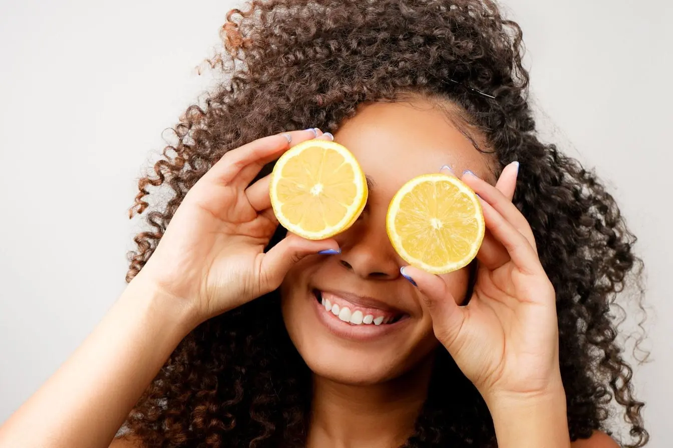 Personne souriante tenant deux moitiés de citron devant ses yeux, image qui illustre l’importance des nutriments comme la vitamine C pour préserver la vision.
