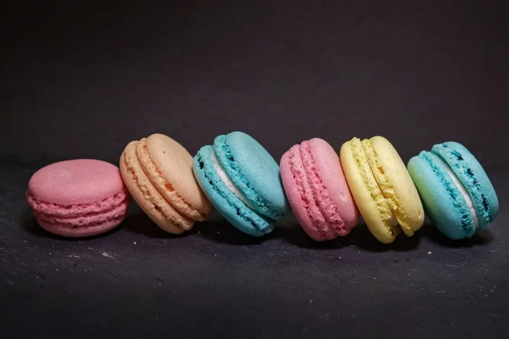 Six macarons aux teintes variées rangés en ligne sur une surface foncée rappellent la gestion des sucres pour la prévention du diabète de type 2.