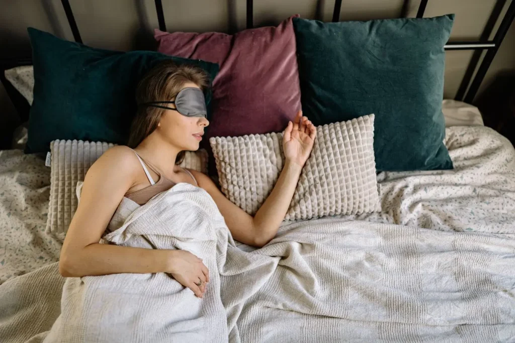 Personne allongée avec masque de nuit et couverture claire, image qui illustre la protection contre la lumière bleue pour préserver un sommeil réparateur.