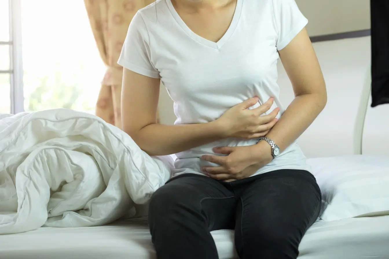 transit intestinal lent Personne assise sur lit tenant son ventre, image qui illustre l’inconfort lié au transit intestinal lent et la recherche de solutions naturelles pour apaiser.
