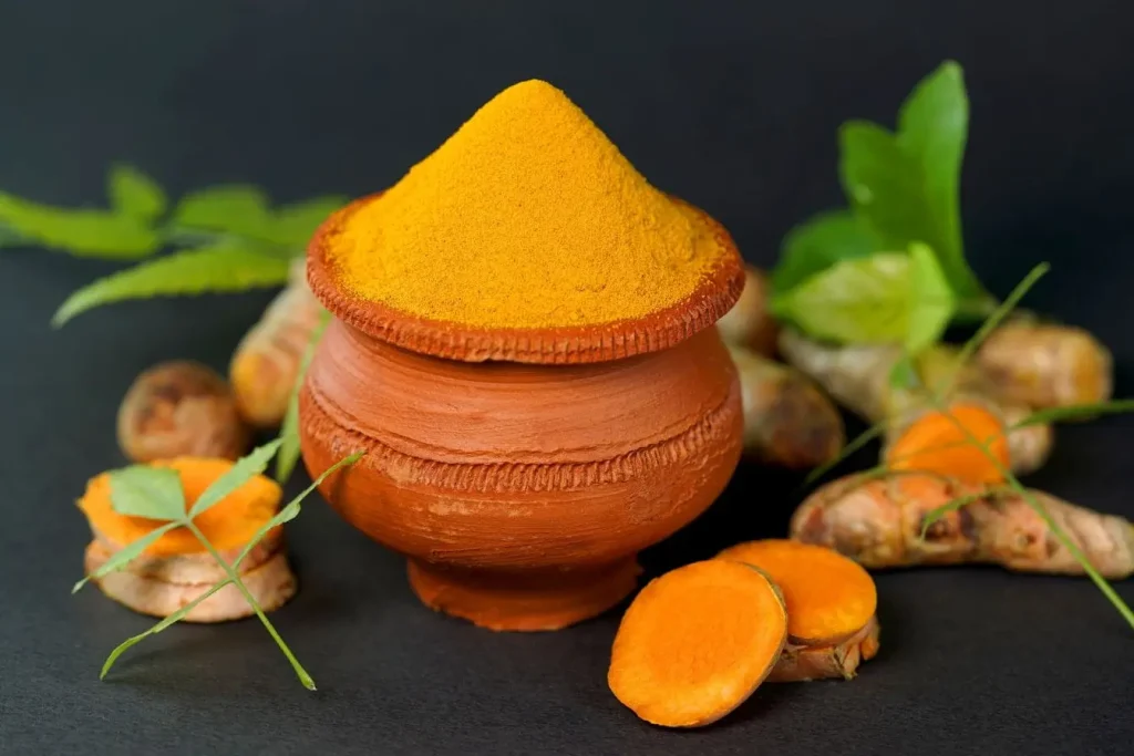 Gros plan sur poudre dorée de curcuma dans récipient brun, image claire illustrant l’importance du poivre noir pour absorber la curcumine.