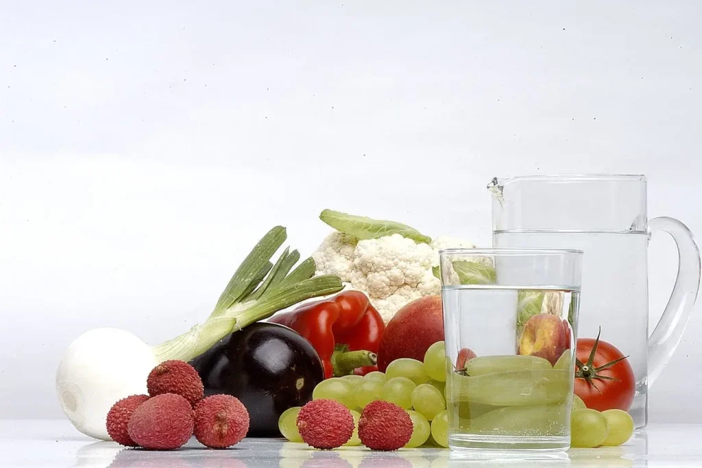 Fruits et légumes frais disposés sur surface blanche avec carafe d’eau, reflet des aliments autorisés et interdits pour la goutte.