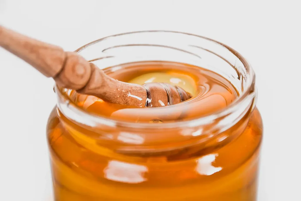 Jarre de miel brillant avec dipper en bois, reflet des bienfaits de la gelée royale et de ses vertus nutritives.
