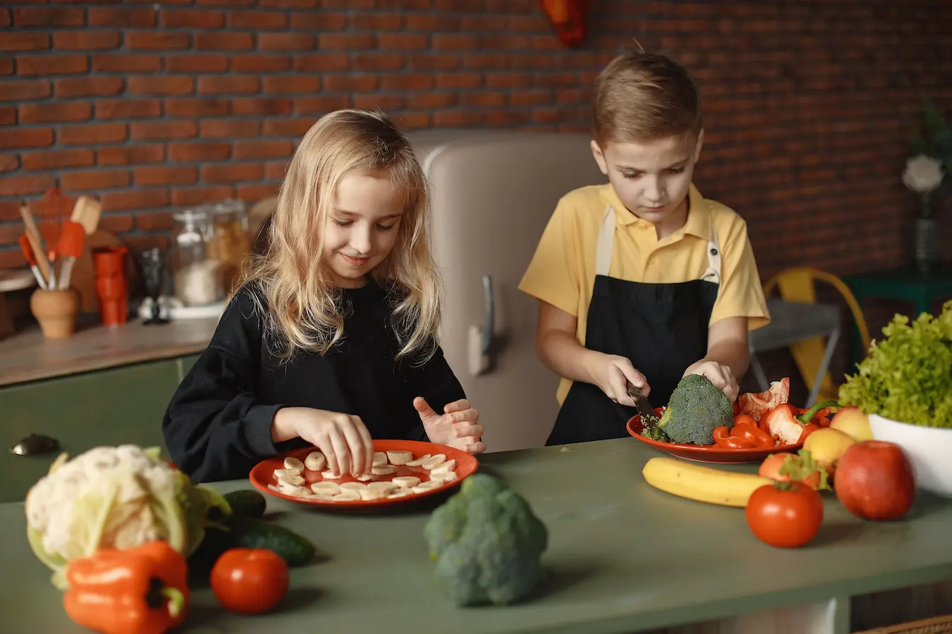 Deux enfants préparent des assiettes de fruits et légumes frais, image qui illustre les aliments riches en mélatonine naturelle pour mieux dormir.