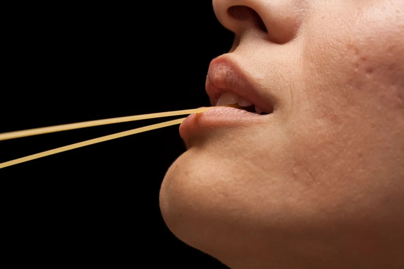 Gros plan sur bouche tenant spaghetti crus, image qui illustre les gerçures aux lèvres.