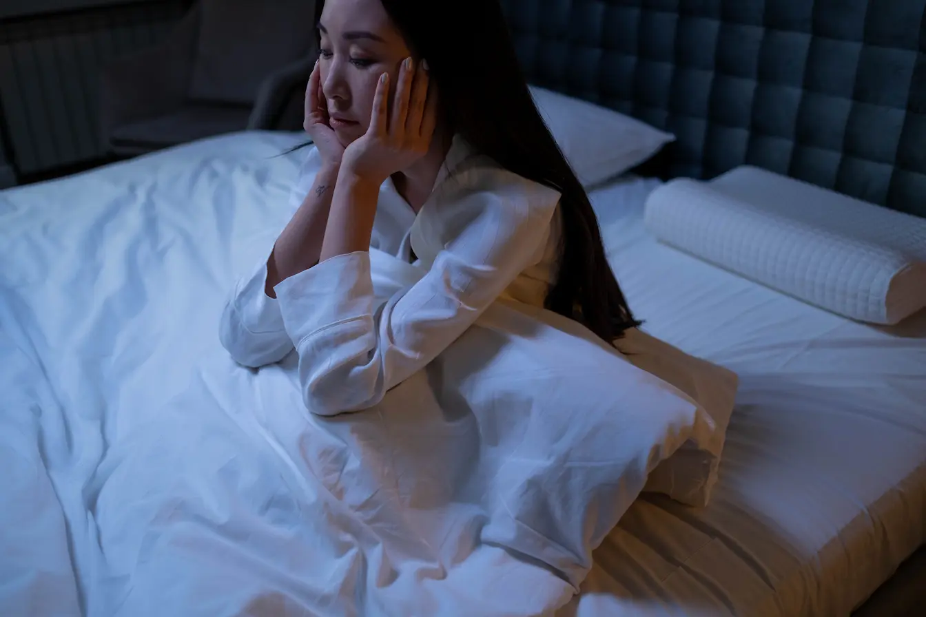 Personne assise sur lit blanc dans ambiance calme, image qui illustre un remède naturel contre l’insomnie.