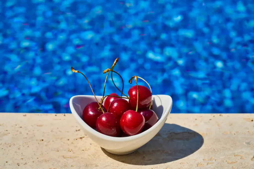 Bol triangulaire rempli de cerises rouges posé près d’une piscine bleue, image qui illustre un remède naturel contre l’insomnie.
