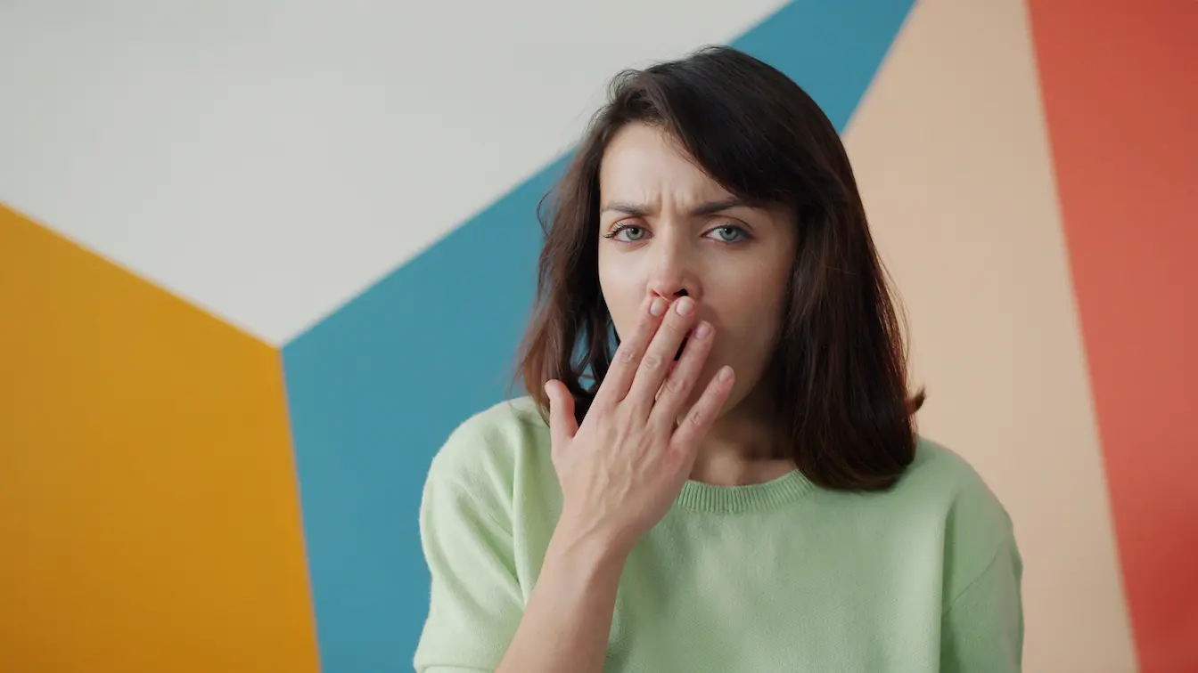 mauvaise haleine Personne en pull vert couvrant bouche avec main, reflet des symptômes liés à la mauvaise haleine d’origine digestive.