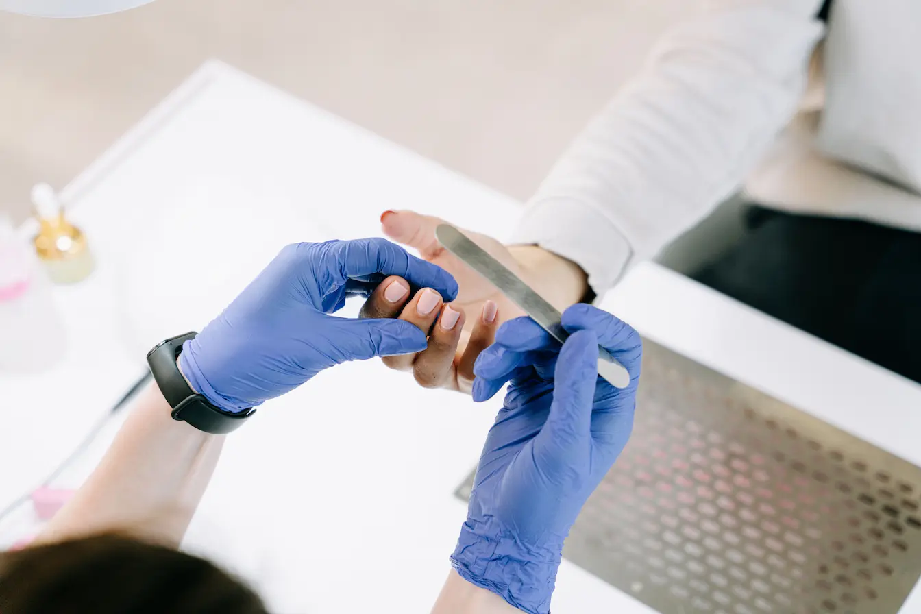 Mains gantées limant ongles vernis rose clair, symbole des soins pour prévenir les ongles cassants et préserver leur santé.