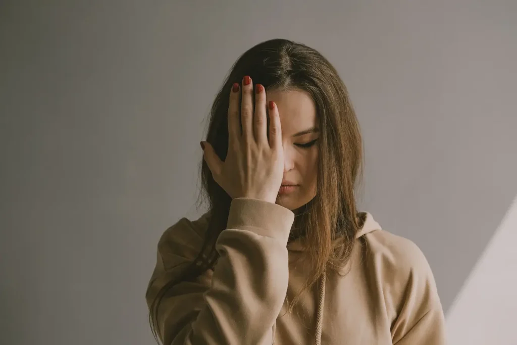 Personne en hoodie beige couvrant ses yeux avec la main, image qui illustre le palming comme remède naturel contre la sécheresse oculaire.