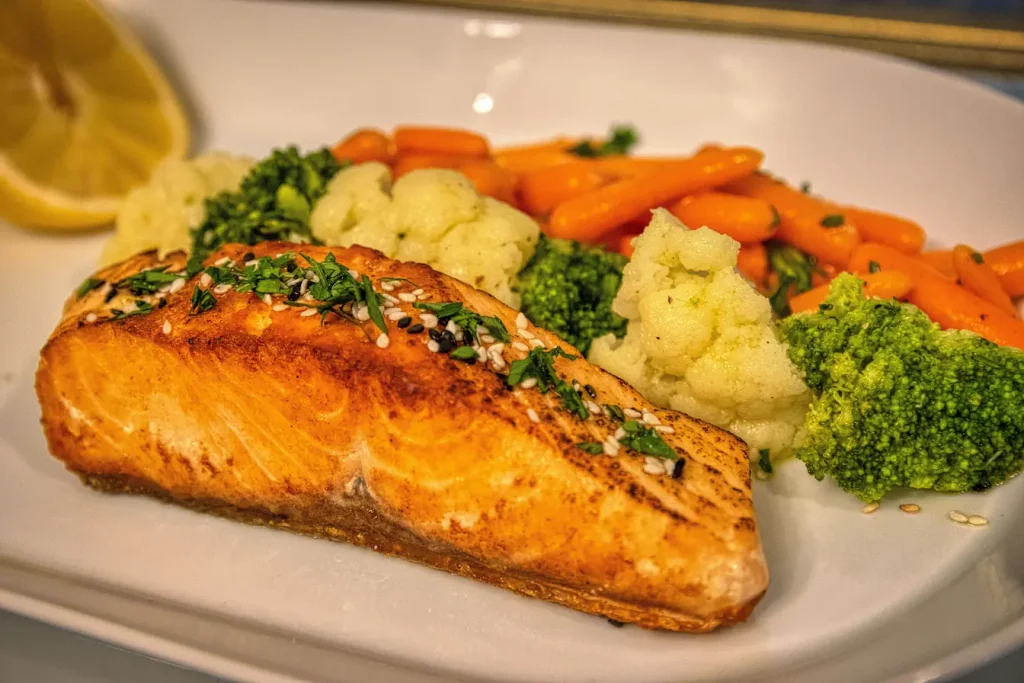 Assiette de saumon grillé avec légumes vapeur colorés, symbole du lien entre alimentation équilibrée et régulation du sébum sur peau grasse.