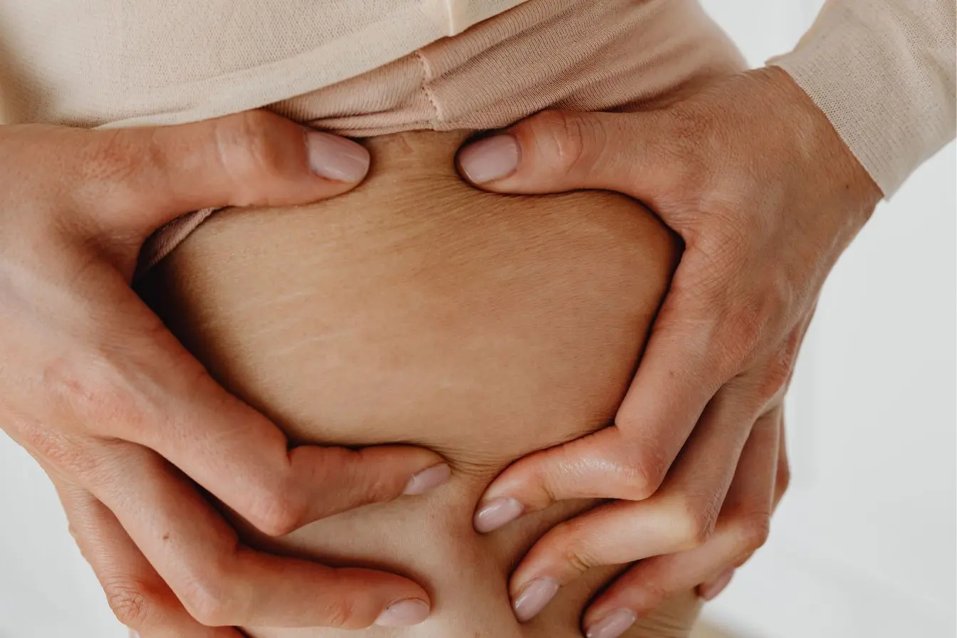 Gros plan sur ventre avec mains pinçant la peau, symbole des préoccupations liées à la cellulite et aux solutions naturelles pour lisser.
