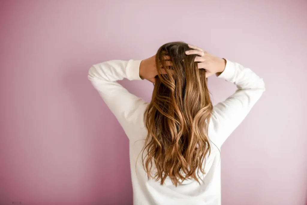 Personne en haut blanc avec cheveux longs ondulés, symbole du déséquilibre capillaire lié aux causes hormonales.