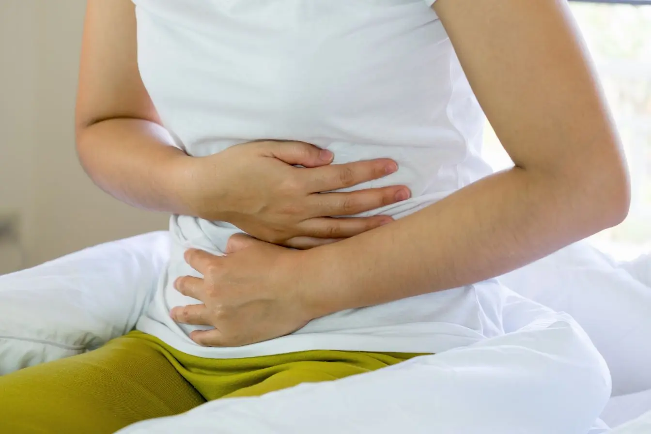 Personne assise sur lit tenant son bas-ventre, symbole des douleurs liées à la constipation chronique.