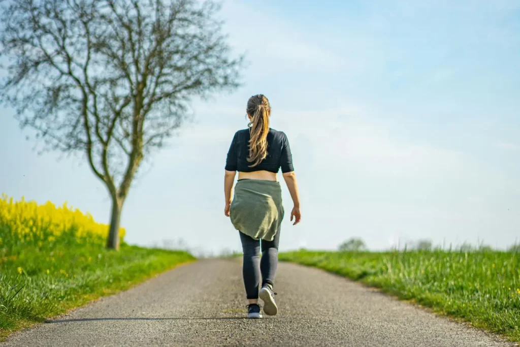 Personne marchant sur chemin pavé entouré de fleurs jaunes, symbole de bien-être et de solutions naturelles pour apaiser les varic