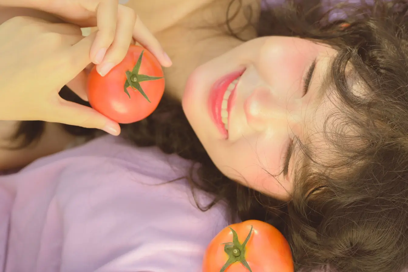 Personne allongée tenant tomate rouge près du visage, symbole du lien entre alimentation et sébum sur peau grasse.
