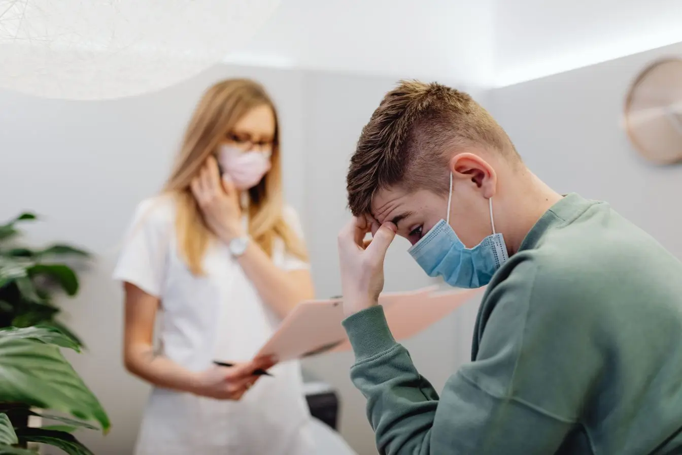 diagnostic de la spasmophilie Une consultation chez le médecin pour un patient masqué qui ressent des malaises, illustrant le diagnostic de la spasmophilie.