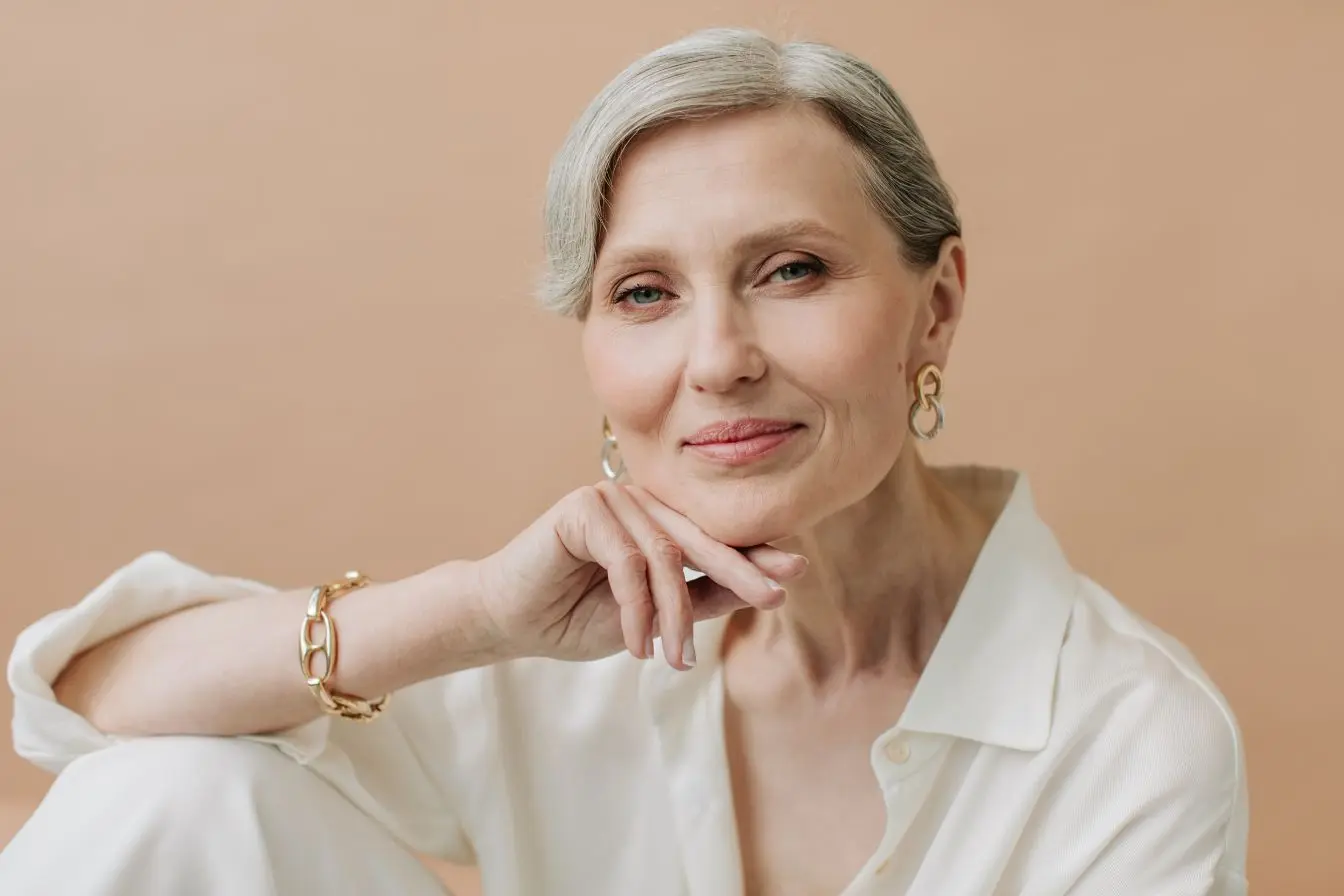 femme aux cheveux gris Portrait d’une femme aux cheveux gris posant dans un décor doux et épuré, illustrant la recherche de remèdes naturels contre les bouffées de chaleur de la ménopause