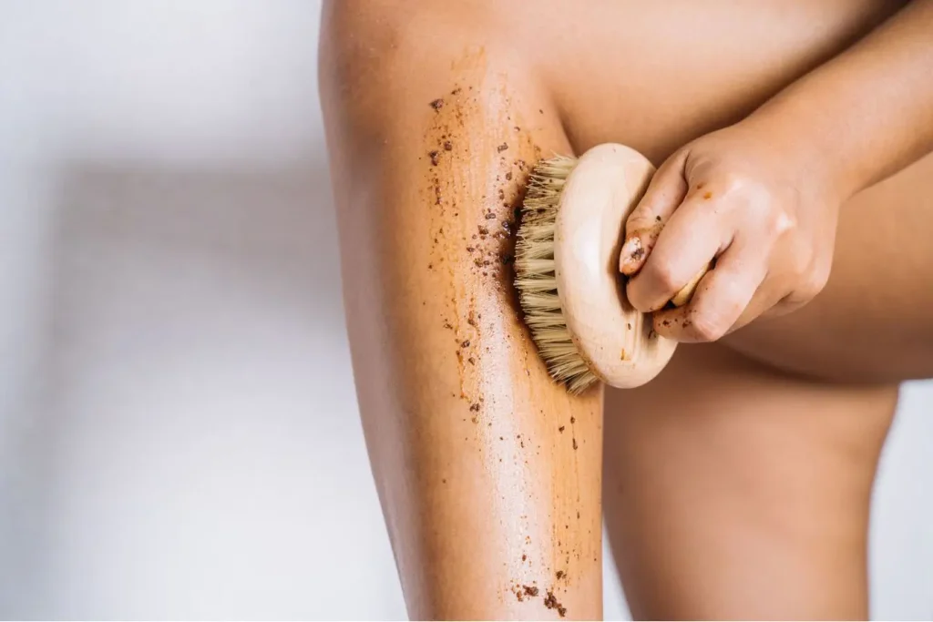 Gros plan sur jambe exfoliée avec brosse ronde en bois, symbole des soins naturels contre la cellulite.