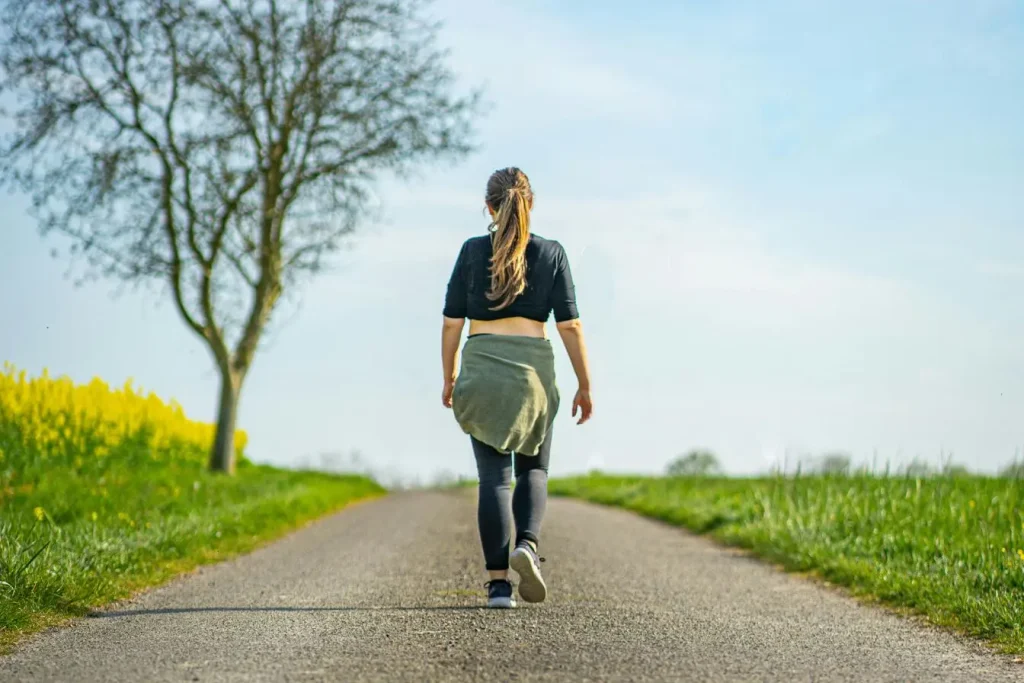Une femme marche seule sur un chemin de campagne bordé de verdure, illustrant les bienfaits des méthodes douces pour apaiser la sciatique.