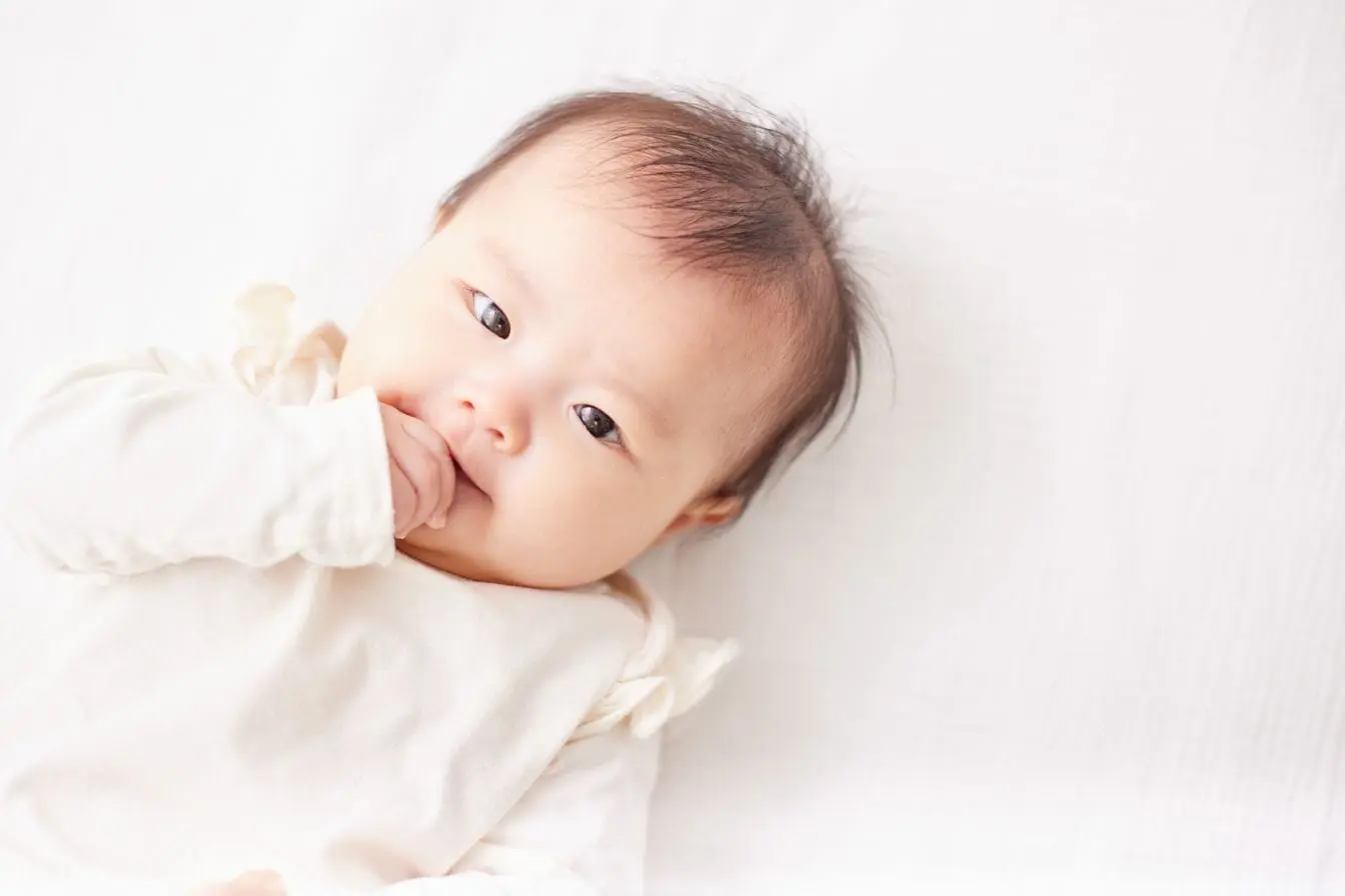 Bébé allongé sur surface claire en tenue douce, symbole des besoins de remèdes naturels pour soulager les coliques.