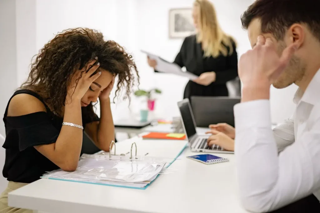 Une femme au bureau plie sous la pression avec les mains sur la tête pendant qu'une crise de stress provoque des palpitations.