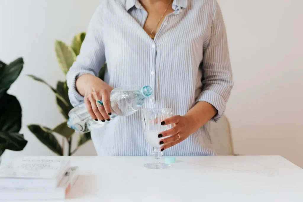 Personne versant de l’eau dans un verre transparent, symbole des remèdes naturels contre la constipation chronique.