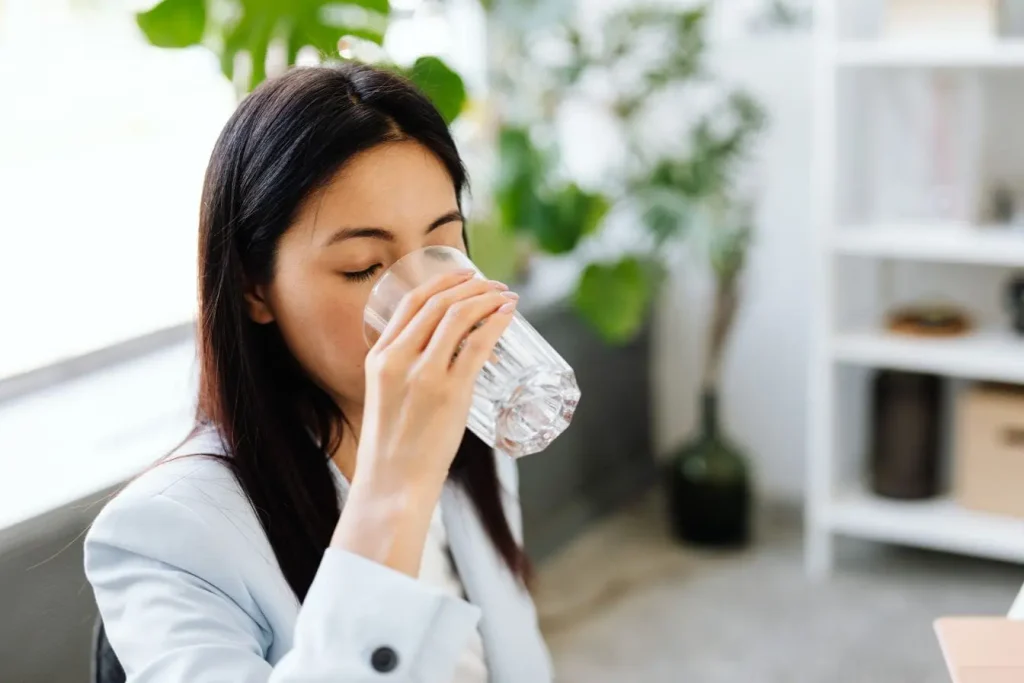 Personne en veste bleue buvant un verre d’eau, symbole des remèdes naturels pour soulager les brûlures d’estomac.